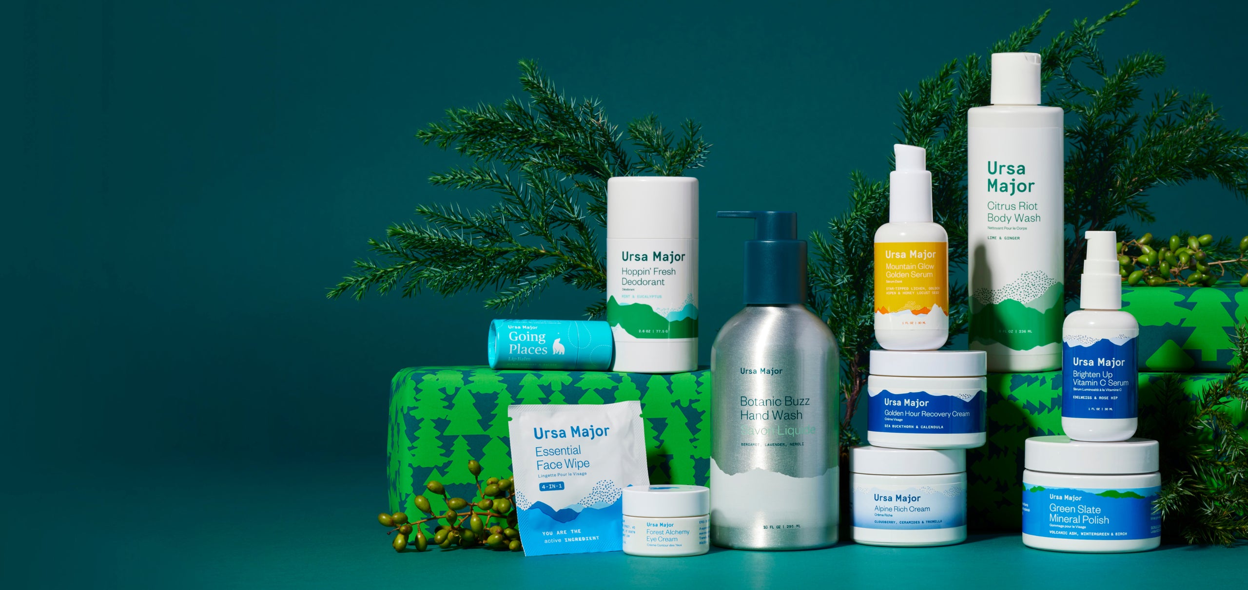 Collection of Ursa Major Skincare products on a dark blue-green background with presents and pine tree limbs around them.