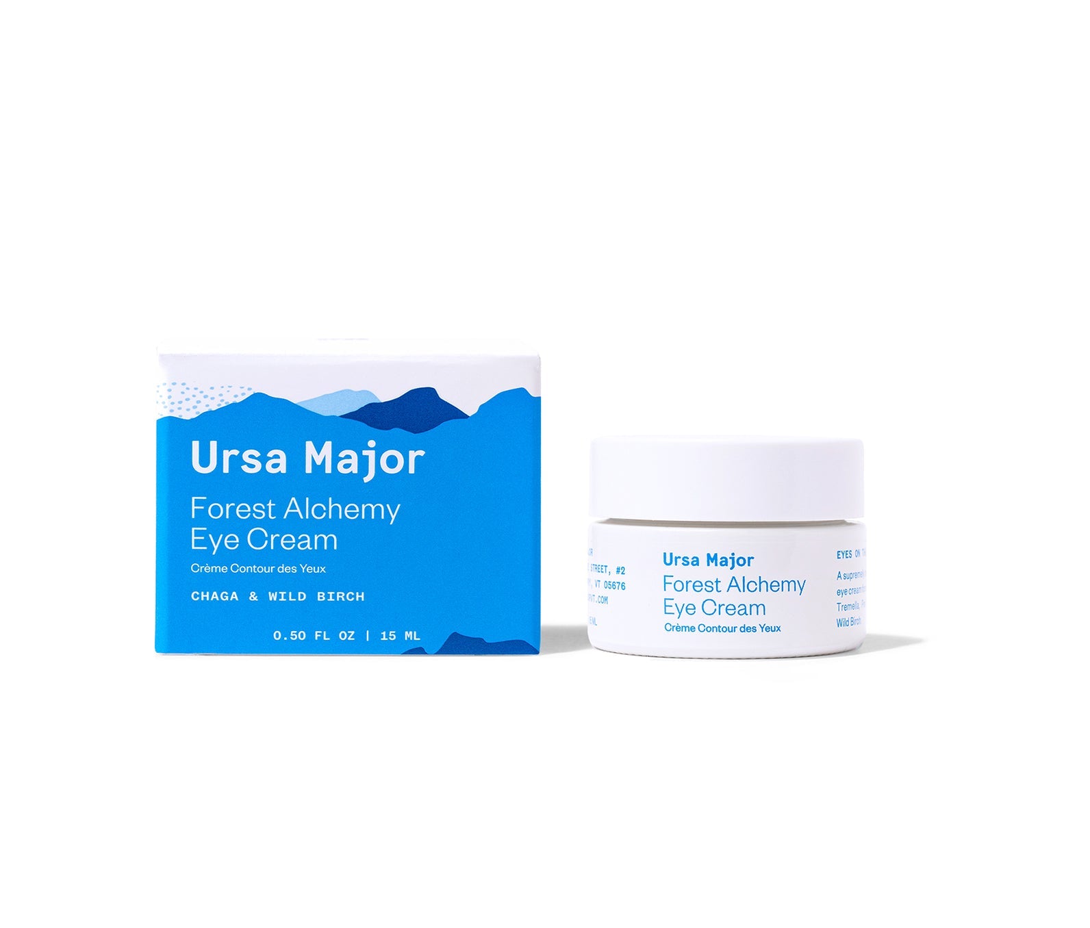 Box of Ursa Major Forest Alchemy Eye Cream next to the jar of eye cream on a white background.  Box has a series of mountains in different shades of blue with white lettering on it.  The jar is white with blue lettering.