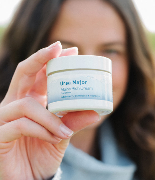 Woman holding a jar of Ursa Major Alpine Rich Cream in front of her face.