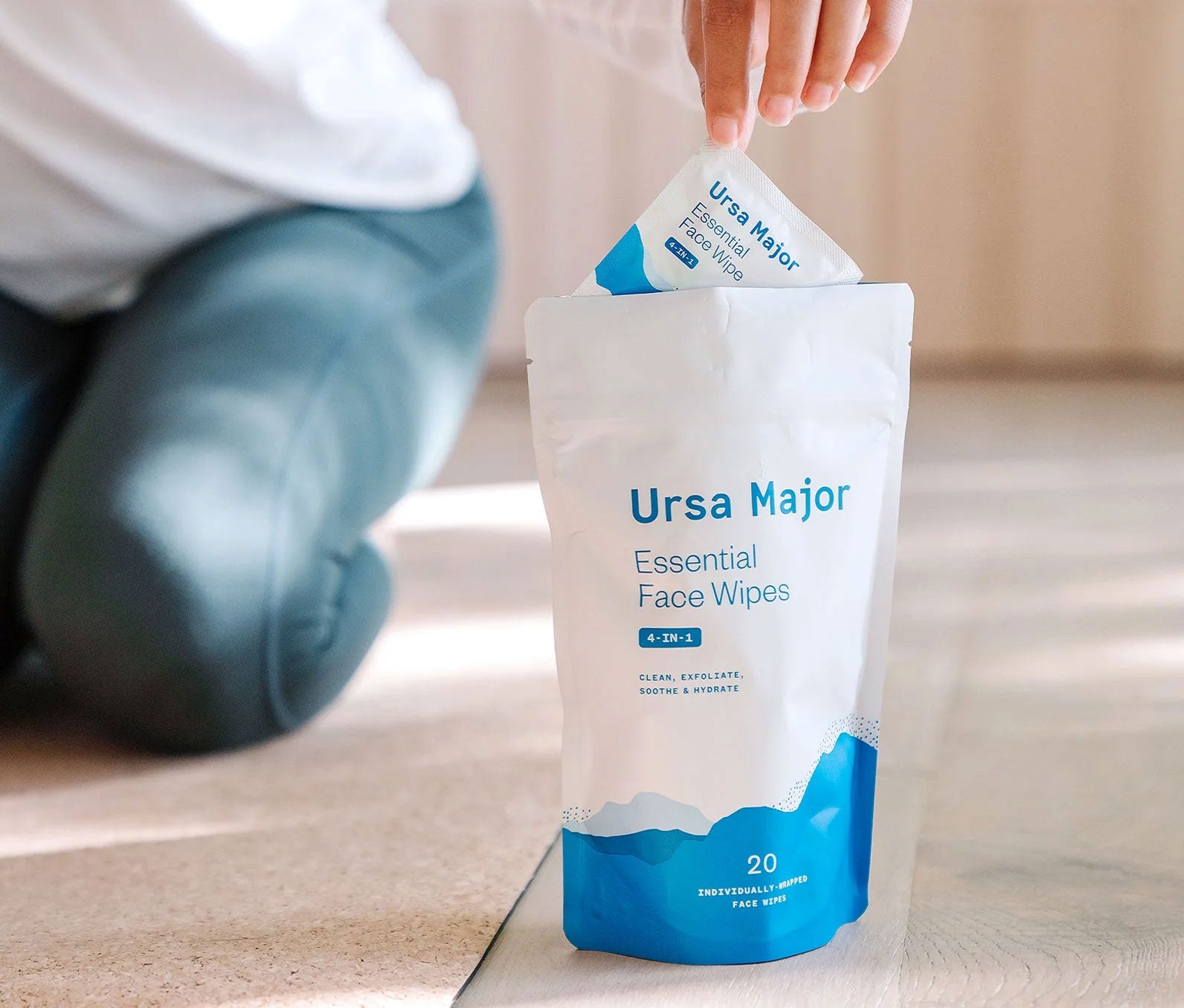 A person removing a single wrapped face wipe from a package of Ursa Major Essential Face Wipes, featuring 20 individually wrapped wipes for face, designed to clean, exfoliate, soothe, and hydrate.