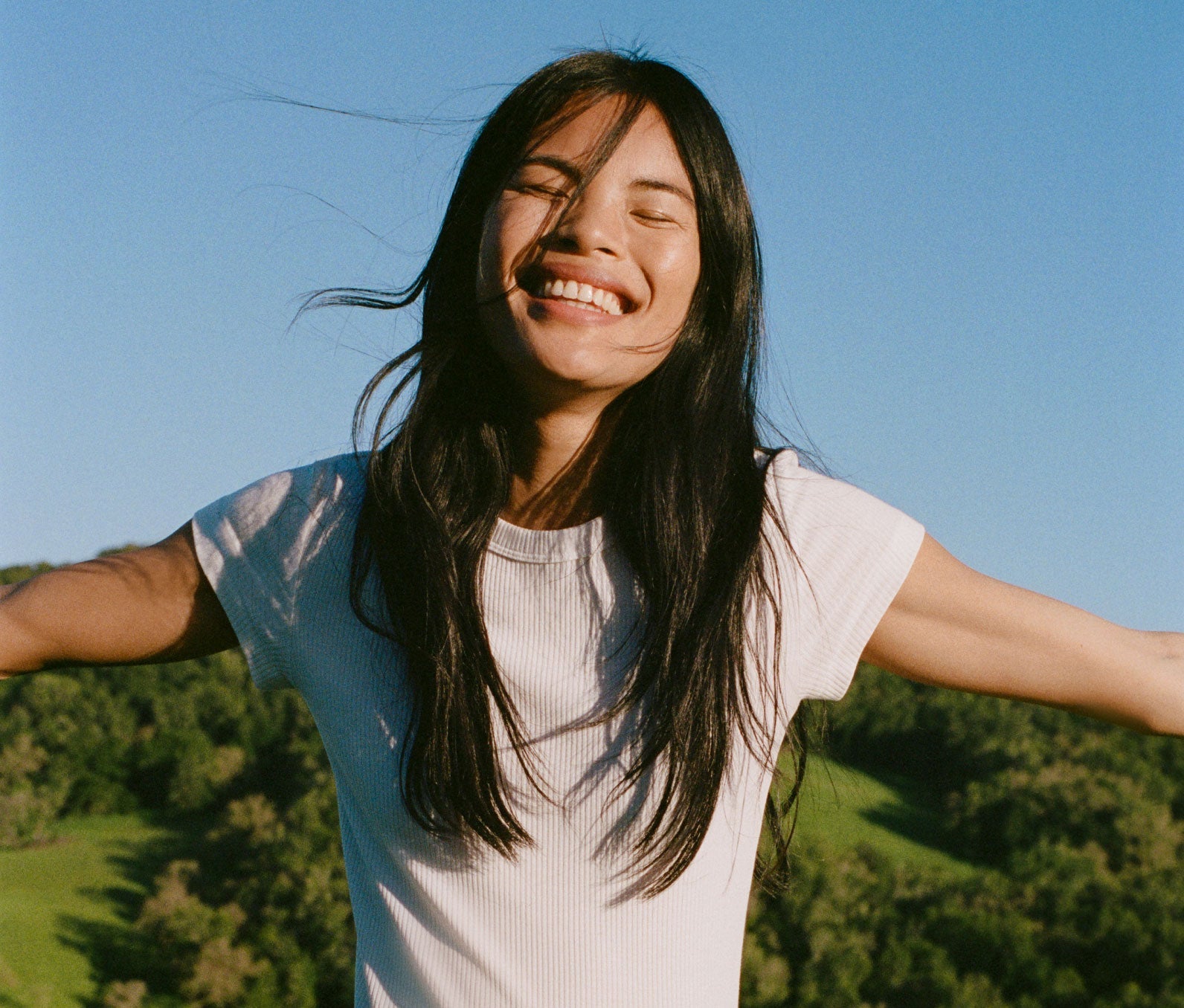 Woman smiling with the sun shining on her face.  She has her arms extended out and her eyes closed.