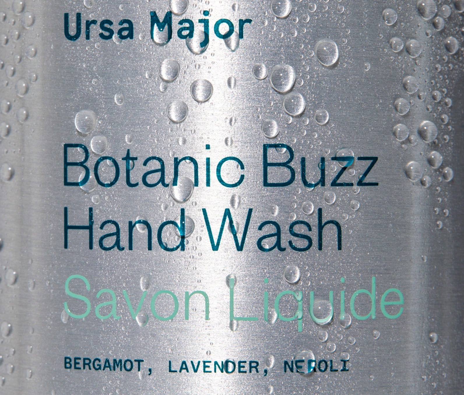 Close-up of Ursa Major Botanic Buzz Hand Wash bottle.  Bottle is aluminum with blue lettering.  This image has water droplets on it.