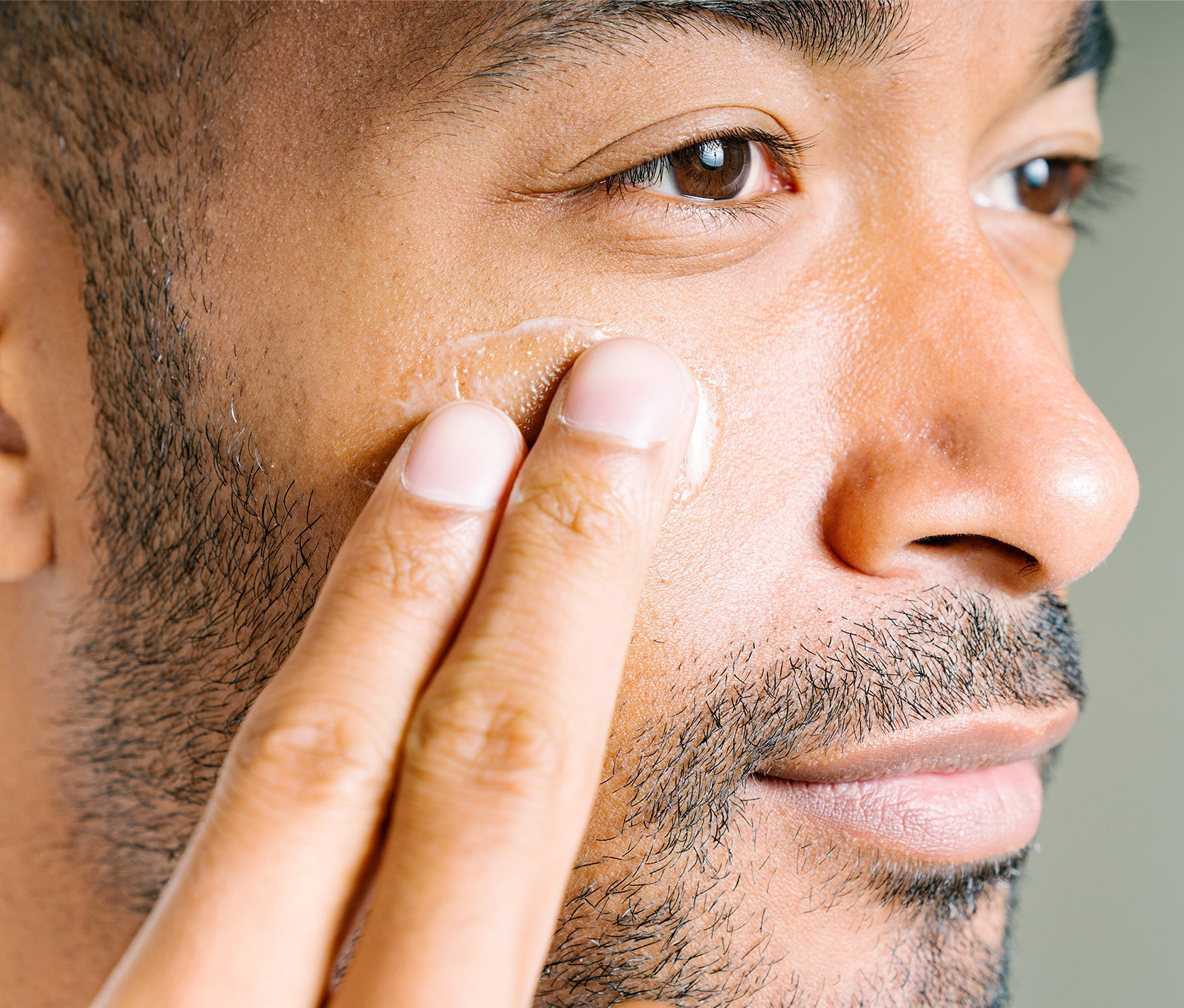 Close-up of a man's face as he swipes Ursa Major Mountain Glow Golden Serum onto his cheek with two fingers.